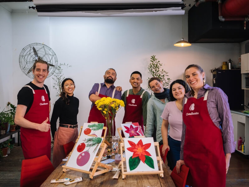 Team smiling behind Christmas paintings on a table